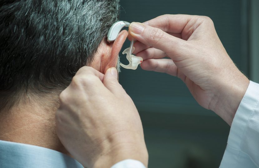 Doctor inserting hearing aid in man's ear